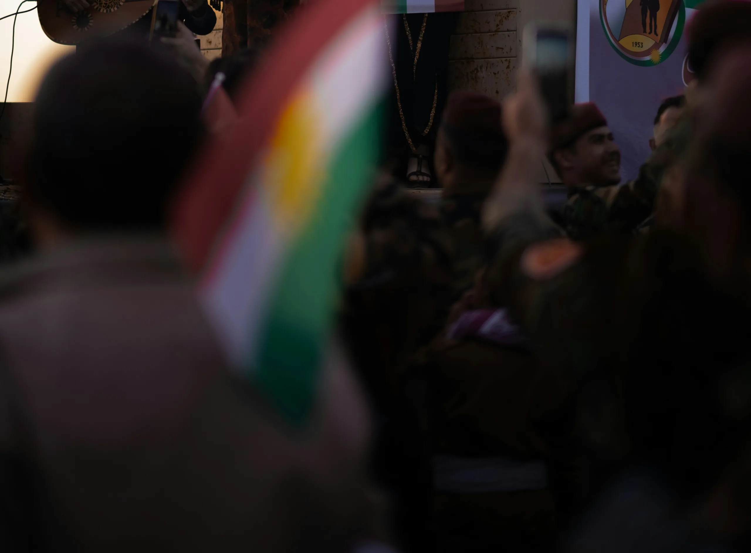 Une homme de dos portant un drapeau Kurde, au premier plan et très flou. L'arriêre plan est net mais très sombre, on ne distingue rien?